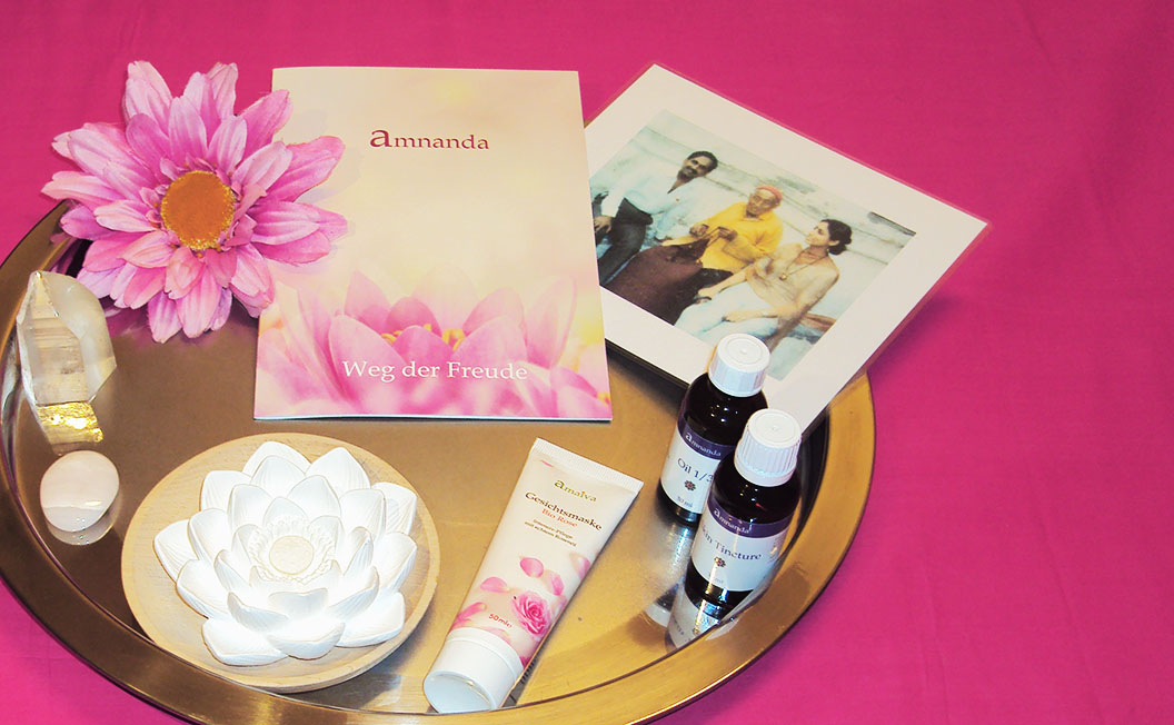 Silbernes Tablett auf pinkfarbenen Tuch, auf dem Tablett befinden sich amnanda-Utensilien: amnanda-Flyer, zwei kleine braune Flaschen, Tube mit Gesichtsmaske, Bergkristall, Duftstein in Form einer Lotusblüte