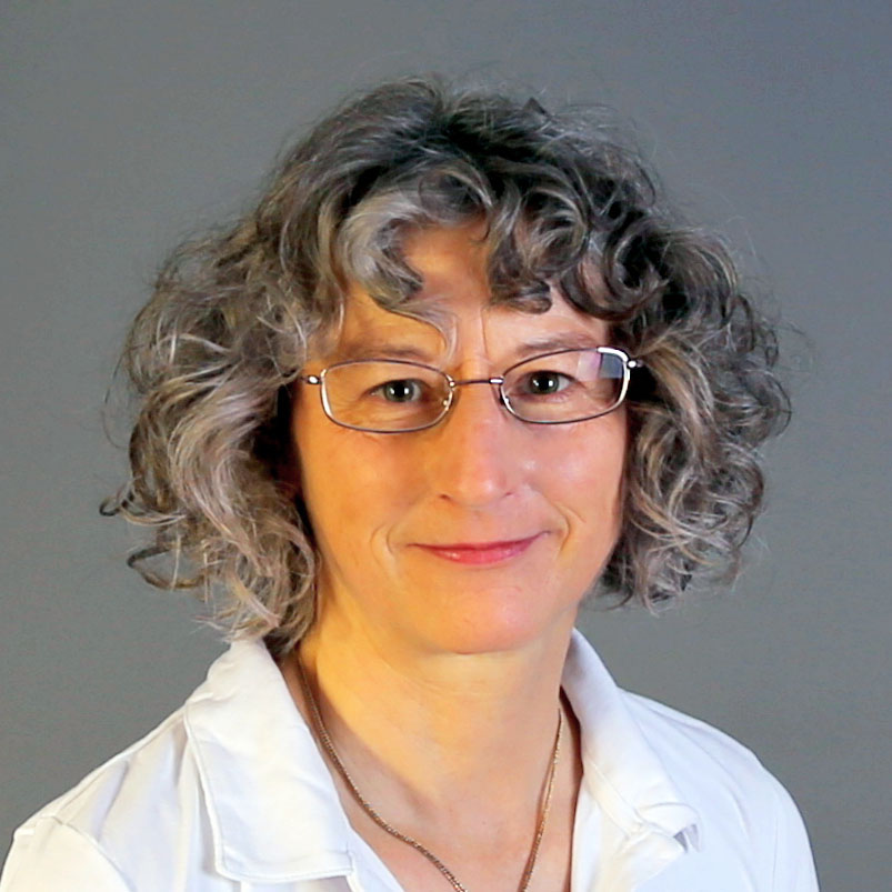 Porträtfoto Waltraud Berchtenbreiter: lächelnde Frau mit schulterlangen grau gelockten Haaren, silberner Metallbrille und weißem Oberteil vor grauem Hintergrund